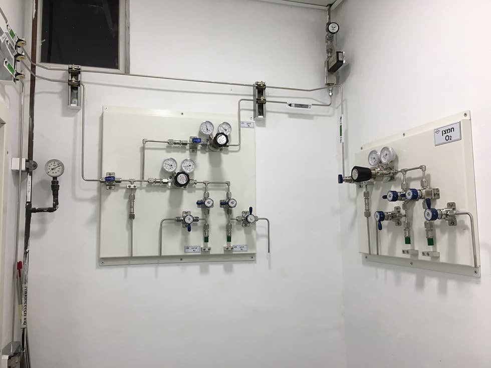 Two white gas panels on a wall with valves and a manifold