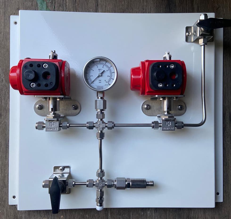 Panel with two red actuated valves and a pressure gauge